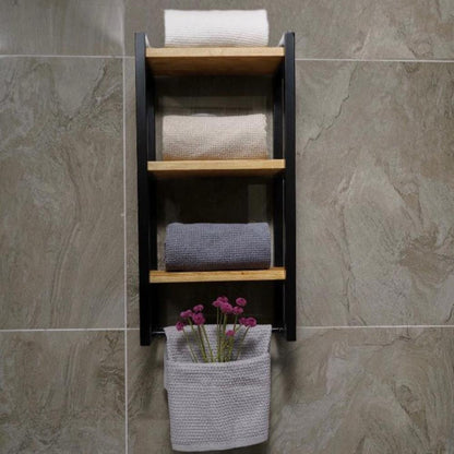 Three-shelf bath towel holder mounted on a stone-textured wall. The organizer features a black metal frame with wooden shelves, displaying folded beige and gray towels.