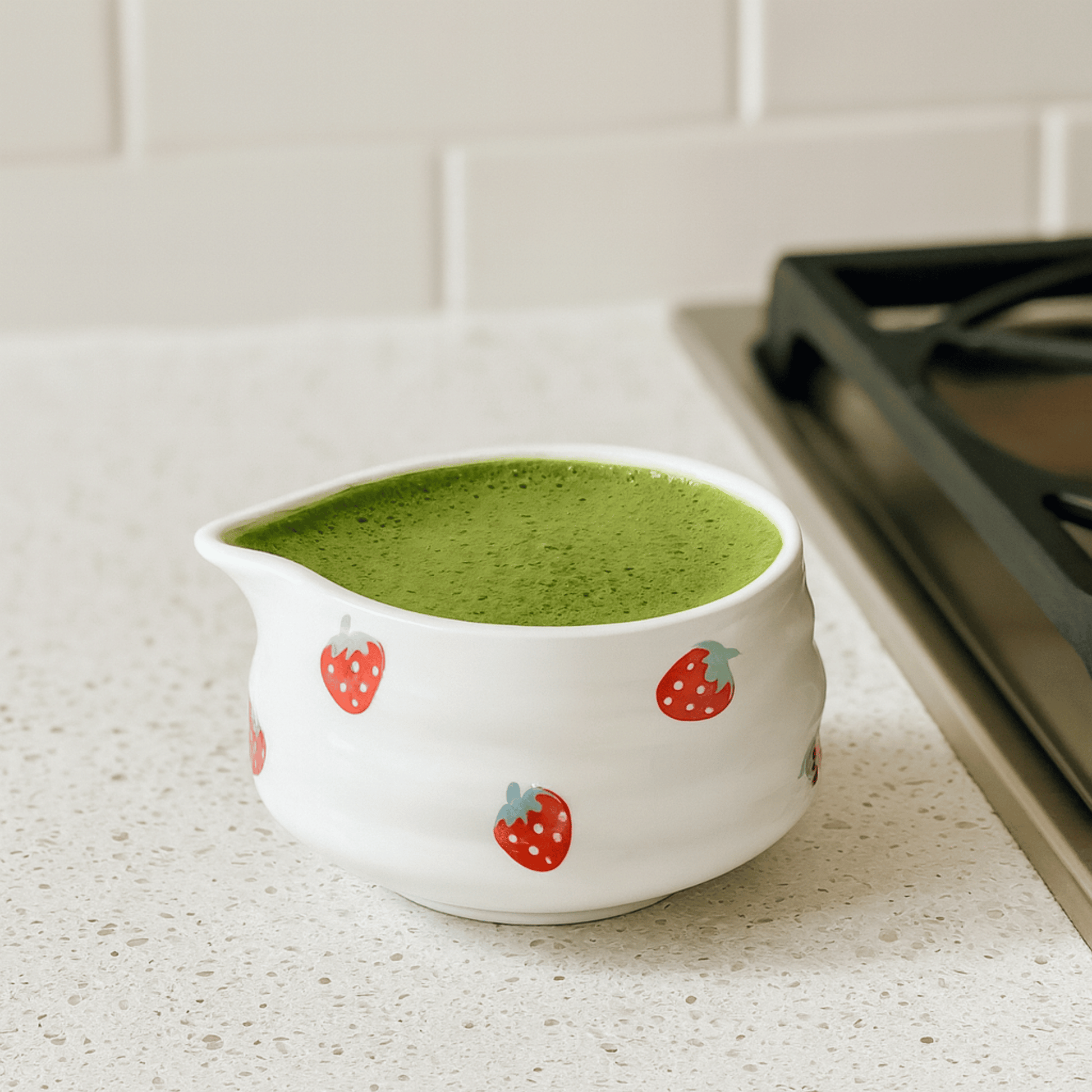 White ceramic pitcher with strawberry design filled with green liquid on a kitchen counter.