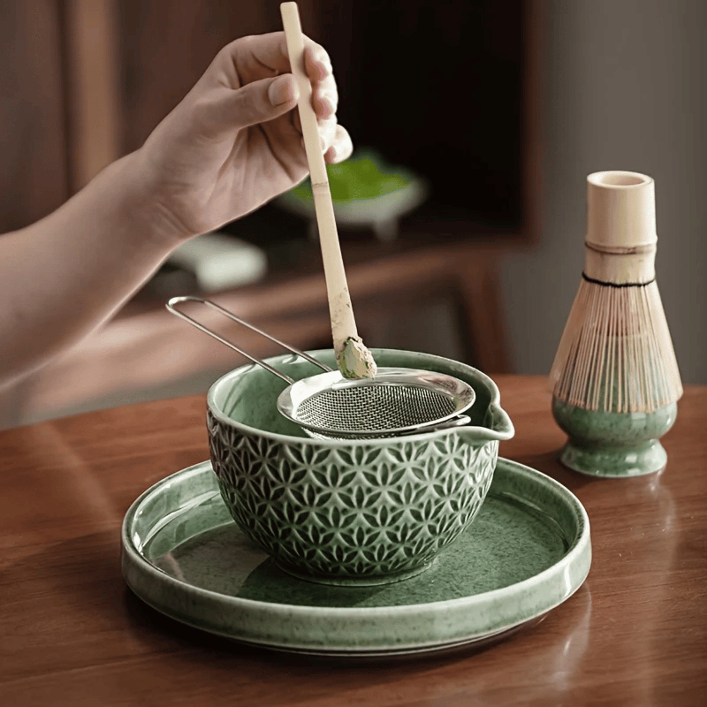 Green ceramic tea bowl with a strainer and wooden spoon on a wooden table.