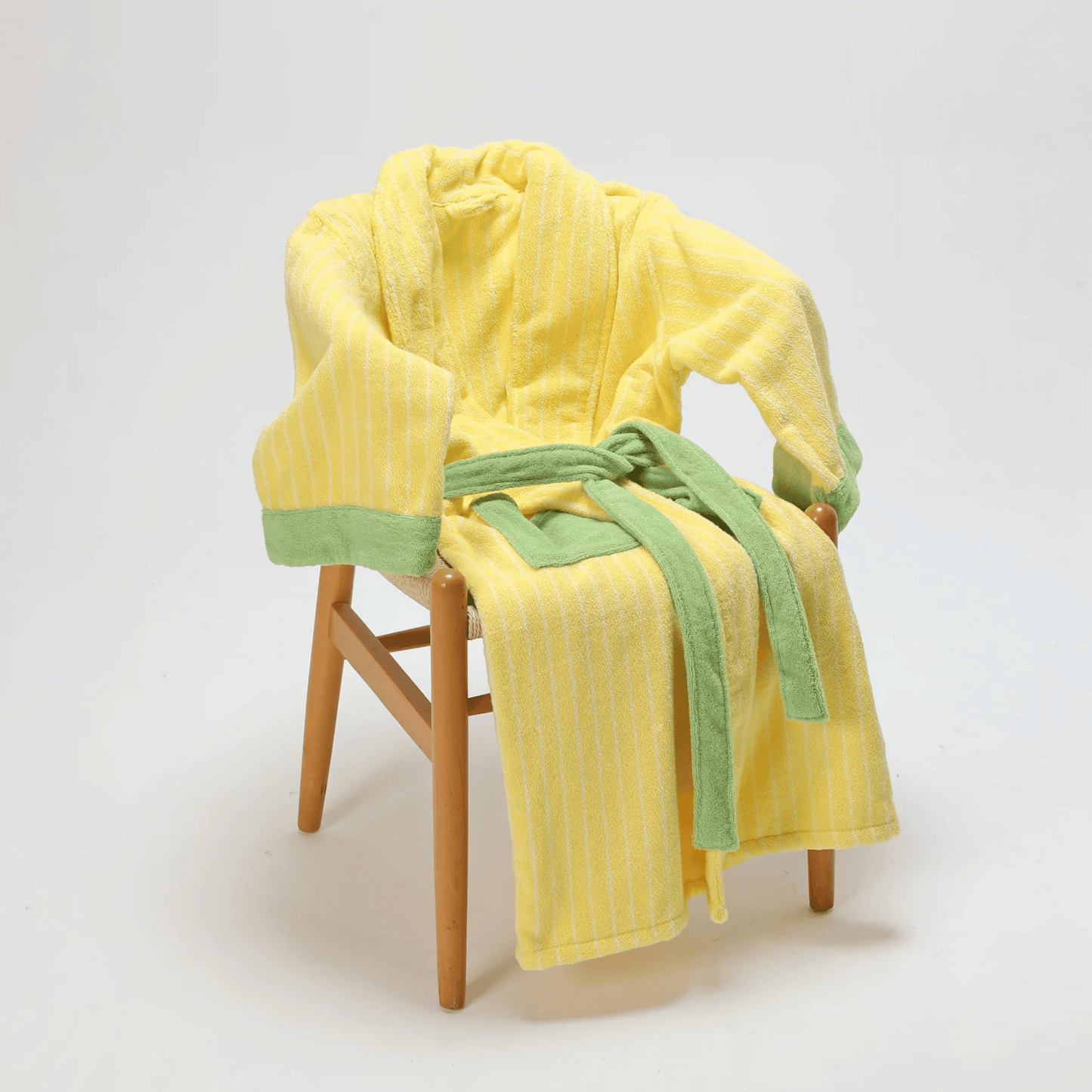 Yellow robe with green trim draped over a wooden chair on a white background