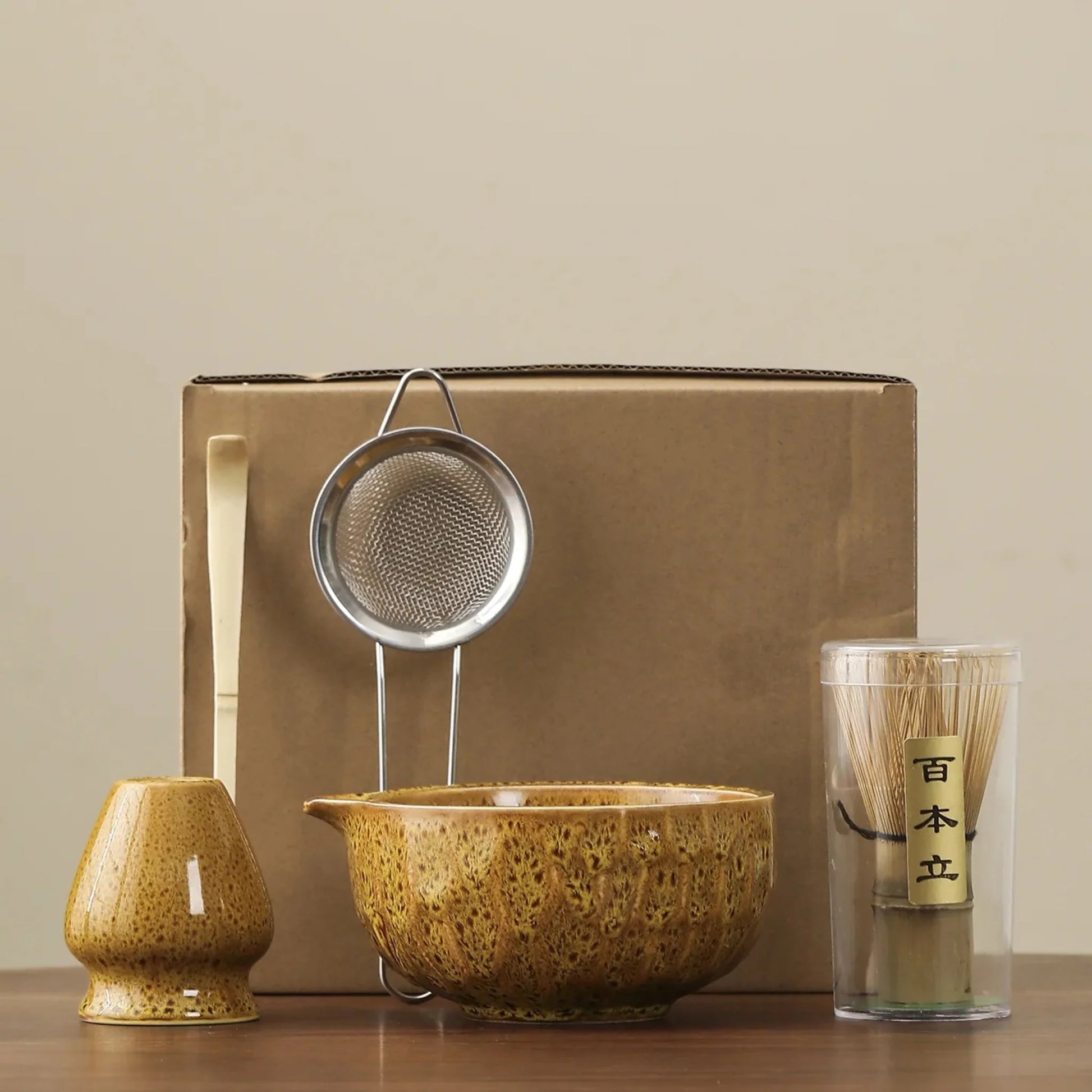 Tea-making set with a bowl, strainer, whisk, and glass on a beige background